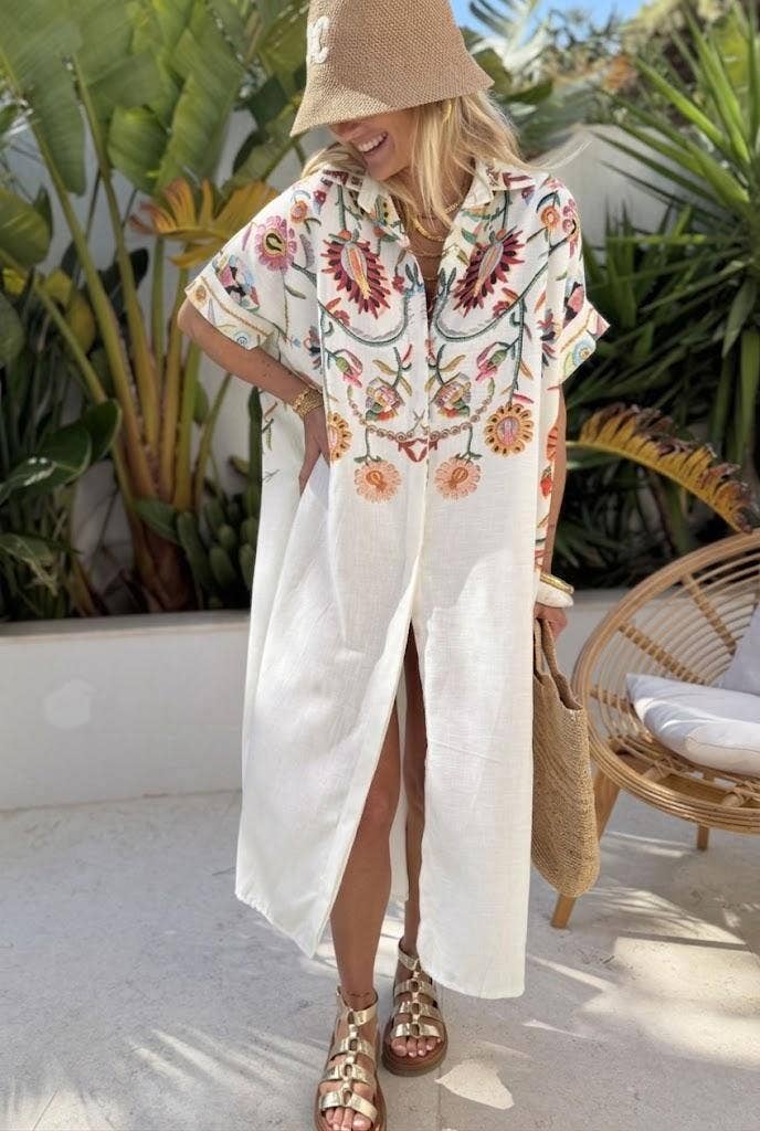 Blonde woman wearing a white kaftan with embroidery on the top half and a straw bucket hat in a tropical location. Found in the resort wear collection from Cita Coastal Resort Wear Boutique.