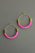 Pink glass beaded hoop earrings with gold accents on a gray background