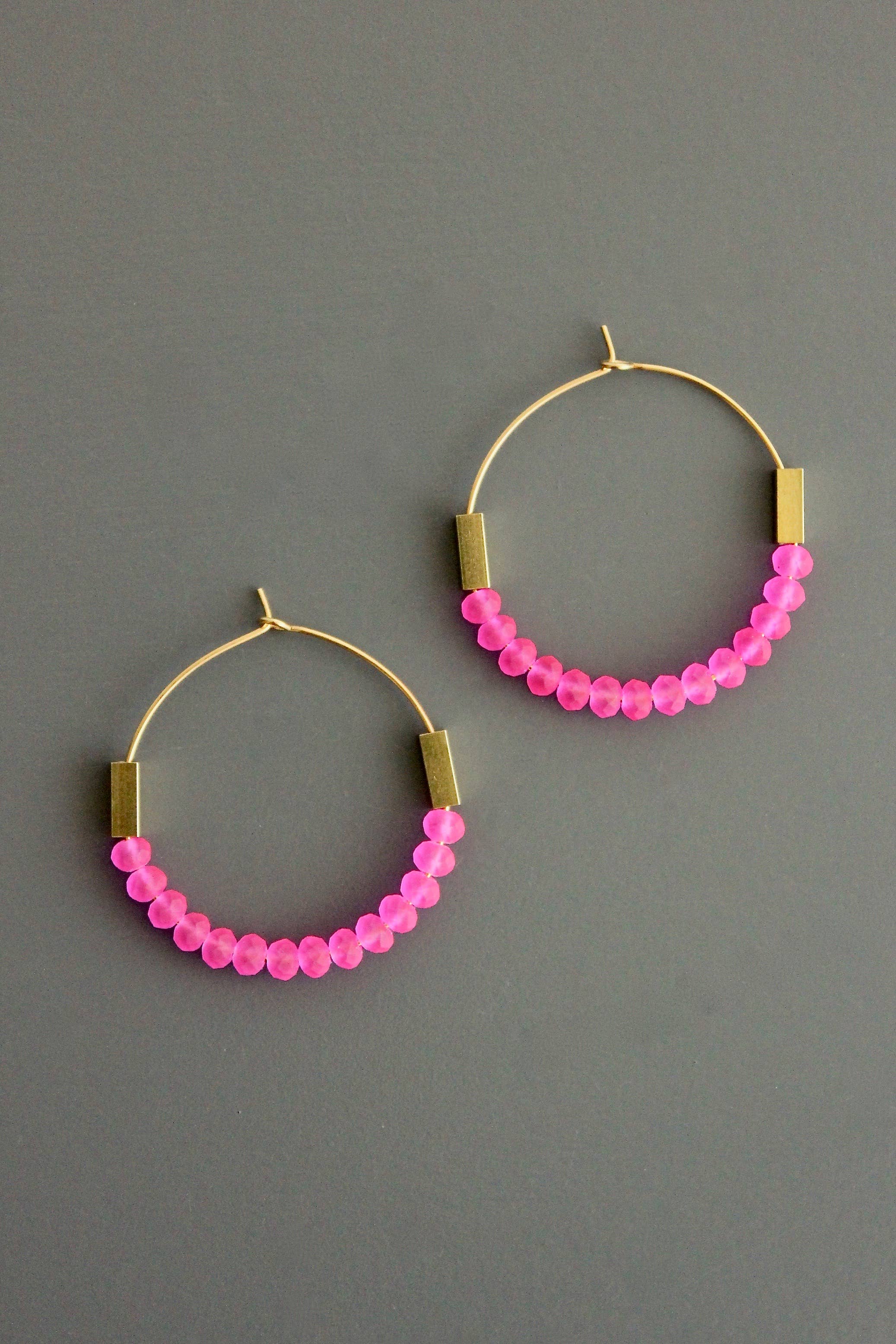 Pink glass beaded hoop earrings with gold accents on a gray background
