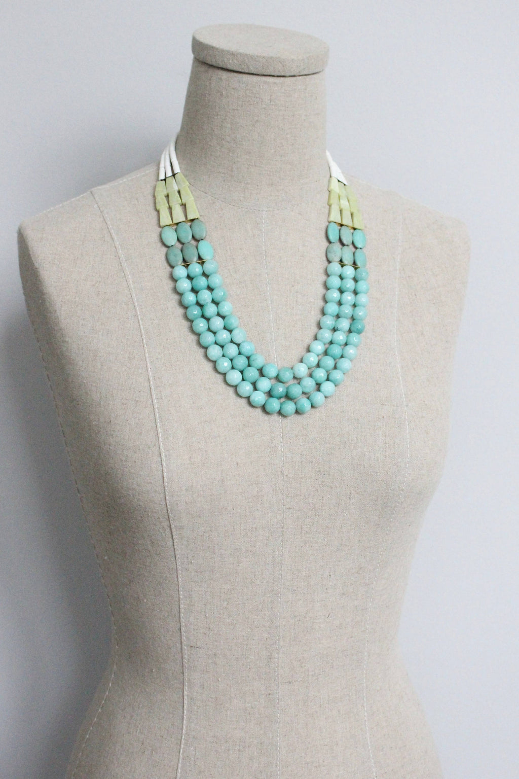 Turquoise beaded necklace on a mannequin bust against a plain background