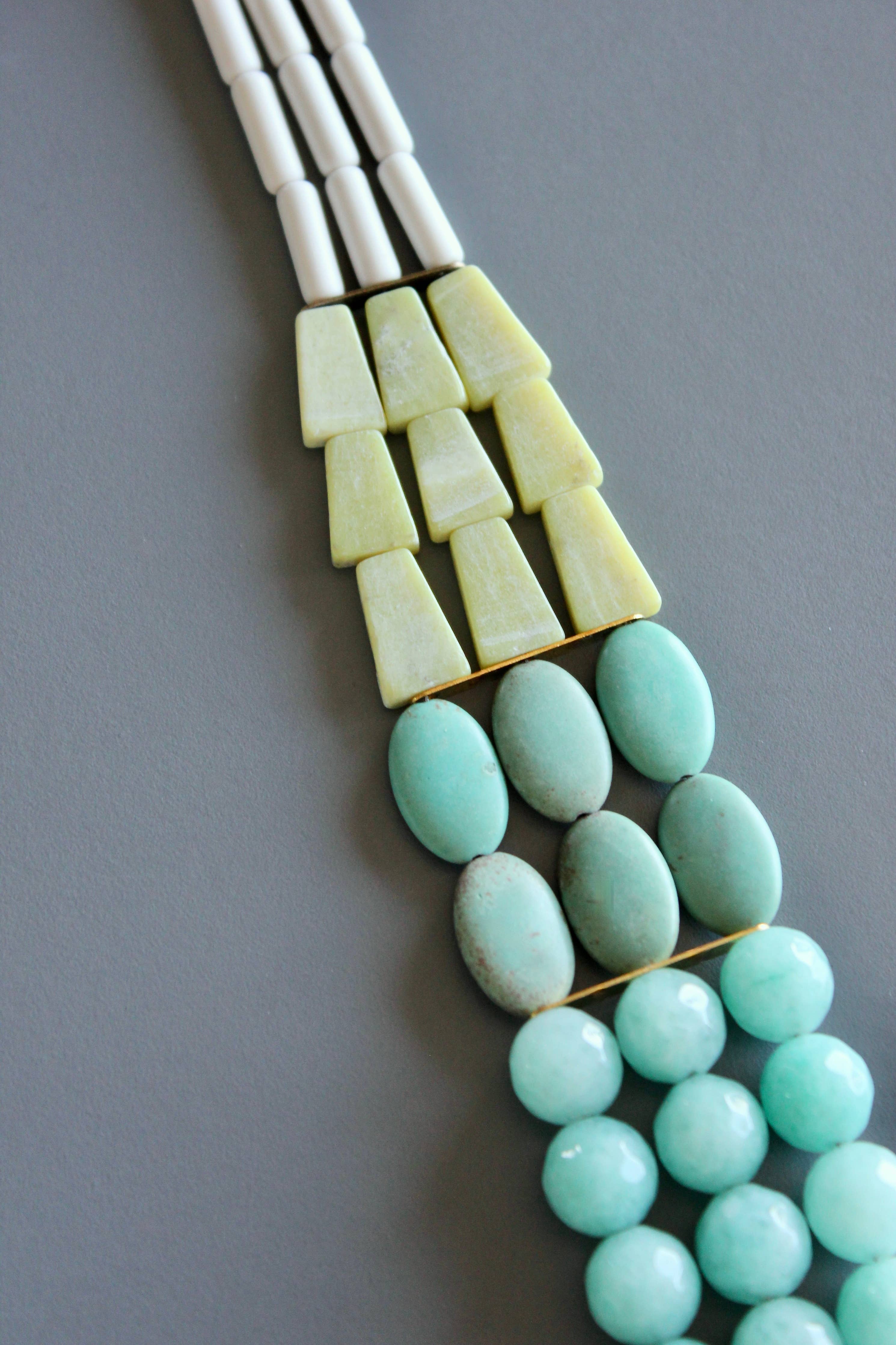 Necklace with green beads and white and beige geometric pendants on a gray background