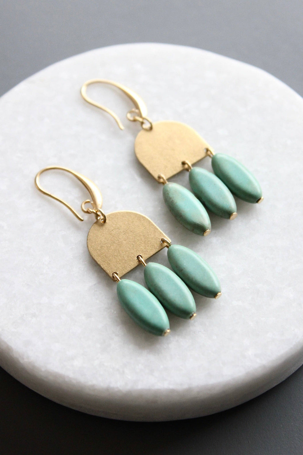 Gold earrings with turquoise beads on a marble surface