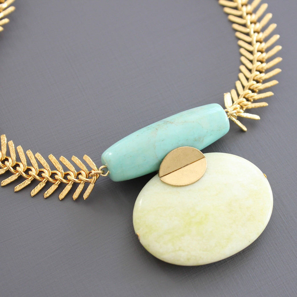 Necklace with gold chain, turquoise stone, and white stone on a gray background